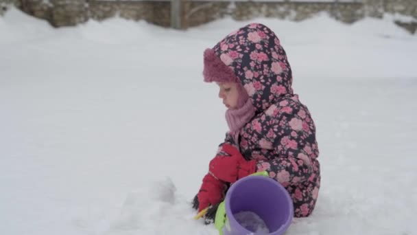 Kış, tatil, oyunlar, aile kavramları. Küçük, otantik anaokulu öğrencilerinin orta planı. Mor elbiseli kız, karla kaplı çayırda kırsalda karla oynuyor. çocuk karlı alanda koşar — Stok video