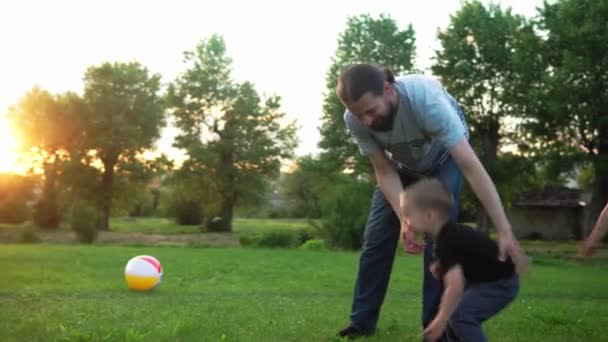 Sommer, Urlaub, Natur, glückliche Familie, Kindheit, Vaterschaft, Vatertag - Papa mit kleinen Vorschulkindern Kinder laufen Spiel haben Spaß an den Händen schwingen mit großen aufblasbaren Ball im Park bei Sonnenuntergang draußen — Stockvideo