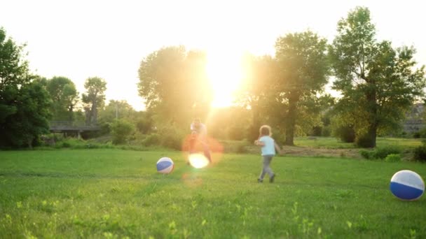 Sommer, Urlaub, Natur, glückliche Familie, Kindheit, Vaterschaft, Vatertag - Papa mit kleinen Vorschulkindern Kinder laufen Spiel haben Spaß an den Händen schwingen mit großen aufblasbaren Ball im Park bei Sonnenuntergang draußen — Stockvideo