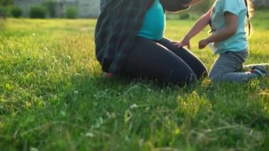 Yaz, doğa, mutlu aile, hamilelik - iki küçük çocuğu olan hamile kadın anne gün batımında parkta çimlerin üzerinde oturuyor. Çocuklar annelerinin karnını okşayıp eğleniyorlar, gülüyorlar birlikte vakit geçiriyorlar.
