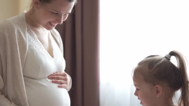 Gravid kvinde føler sig glad derhjemme at tage sig af barnet. Ung vordende mor strøg mave med lille baby datter og kysse mave. Barsel prænatal pleje, graviditet, moderskab koncept. – Stock-video