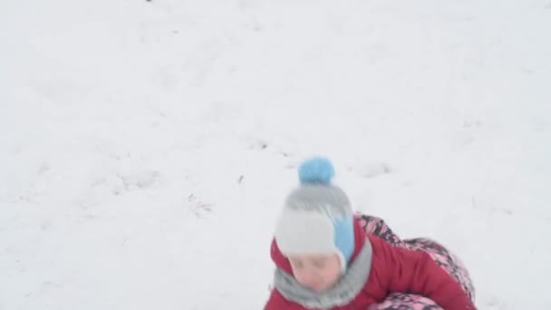 Vacanza, gioco, concetto di famiglia - Slo-mo autentico Due felici bambini in età prescolare fratelli scivolano giù per la collina e si aiutano a vicenda salire. nevicate nella stagione fredda tempo in neve parco invernale all'aperto — Video Stock