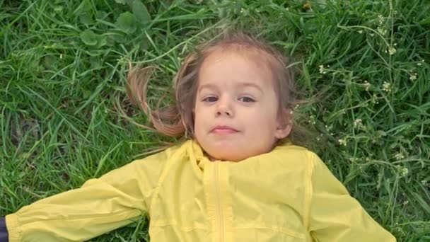 Autêntico bonito pequena menina pré-escolar em amarelo rosa coletar flores no parque rastejando na grama ao pôr do sol da primavera. criança na natureza durante o nascer do sol. Infância, paternidade, família, conceito de estilo de vida — Vídeo de Stock