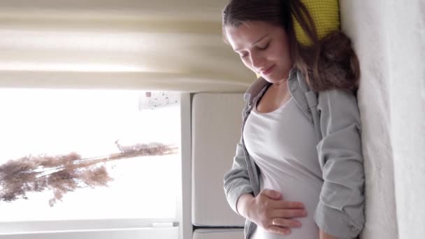 Verticaal Formaat Video van vermoeide zwangere vrouw die buikwandeling aanraakt lig thuis op bed zorgzame moeder neem rust beroerte buik op in zonnige dag. zwangerschap, moederschap, mensen, verwachtingsconcept — Stockvideo