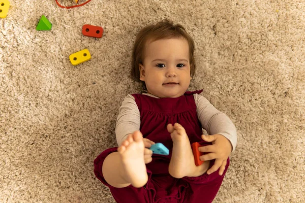 Verzorging, jeugd - bovenaanzicht portret een beetje blij grappig glimlachen authentiek kind peuter kind in roze hebben plezier knuffel benen spelen met vormen liggen op zachte witte vloer mat binnen in gezellige zoete huis — Stockfoto