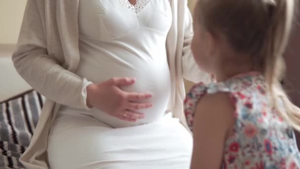 Femme enceinte se sentant heureuse à la maison en prenant soin de l'enfant. Jeune femme enceinte caressant le ventre avec sa petite fille et embrassant son ventre. Maternité soins prénatals, grossesse, concept de maternité. — Video