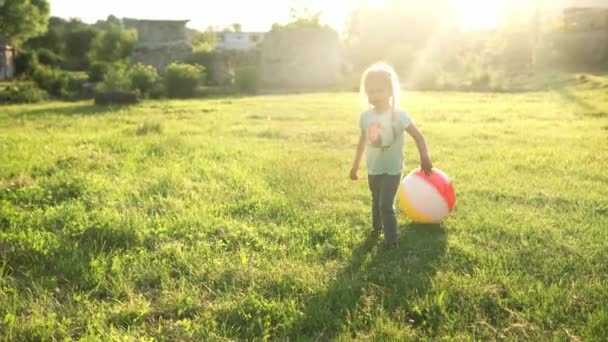 Nyár, nyaralás, természet, boldog család, gyermekkor, barátság - két kis óvodás kisgyerek testvérek futás játék szórakozni nagy felfújható labda fogás a parkban a füvön naplementekor — Stock videók