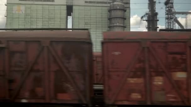 Вид з вікна високошвидкісного поїзда на ландшафті старих іржавих вагонів і сталевих зернових силосів на красивому хмарному блакитному небі на літньому тлі. Транспорт, подорожі, залізниця, дорога, концепція спілкування — стокове відео