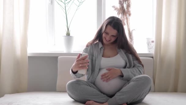 Mujer embarazada feliz con la tableta tienen videollamada utilizando el teléfono inteligente se comunica con el marido a través de chat consulta en línea con el médico hablar con amigos en el teléfono móvil. embarazo, tecnología, medicina — Vídeos de Stock