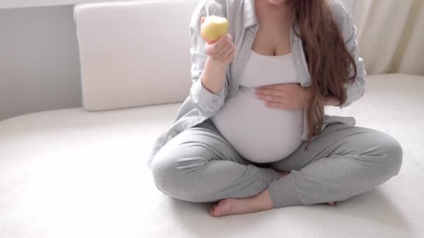 Auténtica linda mujer embarazada sintiéndose feliz en casa con vientre. Joven madre acariciando la barriga y comiendo rojo en un sofá blanco cerca de la ventana. Atención prenatal de maternidad, embarazo, maternidad, concepto de estilo de vida — Vídeos de Stock