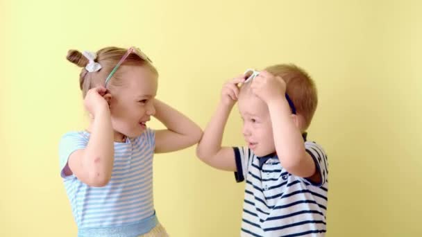 Família, amizade, infância, compras de roupas de verão. Dois felizes sorrindo criança crianças dança irmão celebrar jogo divirta-se rindo. Crianças engraçadas usando óculos de sol no espaço de cópia amarelo — Vídeo de Stock