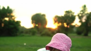 Yaz, tatil, doğa, mutlu çocukluk - pembe şapkalı, gülümseyen küçük bir anaokulu çocuğu kameraya poz veriyor ve gün batımında çayırda büyük bir şişme ile oynuyor.