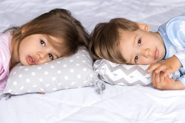 Hogar, comodidad, infancia, insomnio, insomnio, dulce sueño - dos tristes niños cansados niños hermanos gemelos en pijama mentira descanso no puede dormir en la cama almohadas mirar a la cámara suave y acogedor estado de ánimo soñoliento — Foto de Stock
