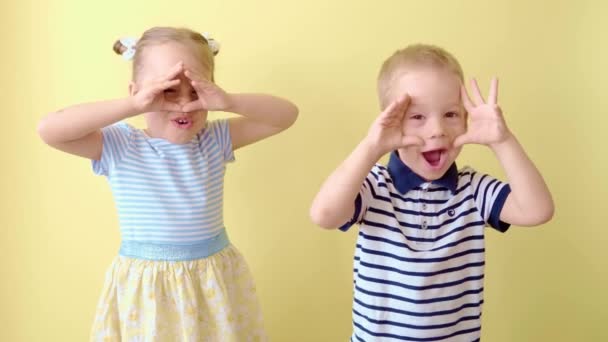 家族友情子供時代夏。2つの幸せな笑顔の幼児の子供の兄弟は、手で目、耳、口をカバージェスチャーを示しています。面白いです子供で眼鏡兄妹上の黄色コピースペース背景 — ストック動画
