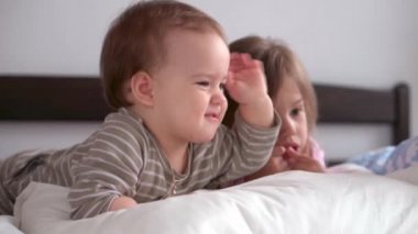 Otantik 3 küçük anaokulu çocuğu reşit olmayan çocuklar, kardeşler akıllı telefon cihazıyla çizgi film izliyorlar evde beyaz yatakta bebek gibi. Aile, eğlence, çocukluk, arkadaşlık konsepti..