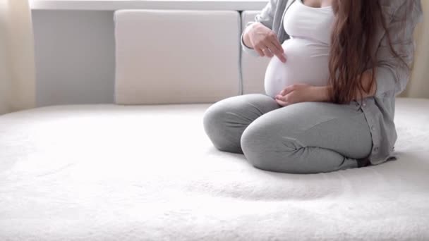 Gravidez, maternidade, pessoas, conceito de expectativa - mulher grávida feliz tocando sua barriga na cama em casa cuidar mãe acaricia grande barriga nua com as mãos, na sala de luz no dia ensolarado de verão — Vídeo de Stock