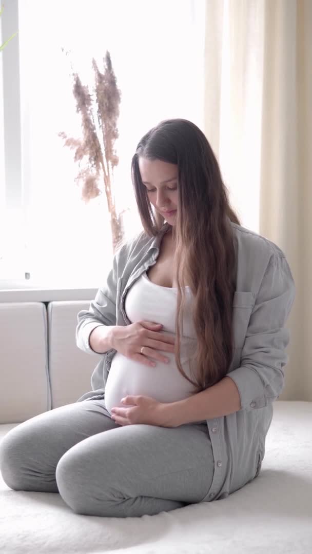 Vertical Format Video de una mujer embarazada feliz tocando la barriga en la cama en casa madre cariñosa acaricia la barriga grande del vientre con las manos en un día soleado de verano. embarazo, maternidad, personas, concepto de expectativa — Vídeo de stock