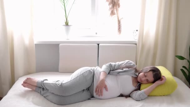 Εγκυμοσύνη, μητρότητα, άνθρωποι, προσδοκία έννοια - ευτυχισμένη κουρασμένη νυσταγμένη έγκυος γυναίκα που αγγίζει τον ύπνο της κοιλιάς ξεκουράζεται στο κρεβάτι στο σπίτι φροντίδα μητέρα λάβει μια κοιλιά εγκεφαλικό επεισόδιο στο φως δωμάτιο στην ηλιόλουστη μέρα — Αρχείο Βίντεο
