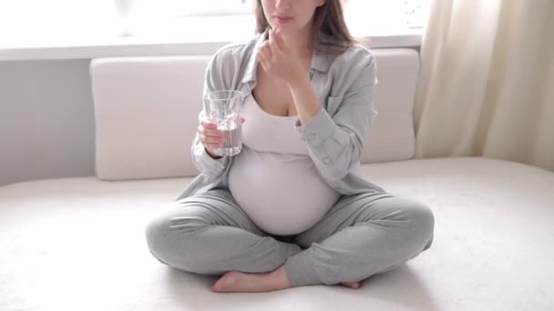 Auténtica linda mujer embarazada sintiéndose feliz en casa con vientre. Joven madre acariciando barriga y beber agua de vidrio cerca de la ventana. Atención prenatal de maternidad, embarazo, maternidad, concepto de estilo de vida — Vídeos de Stock