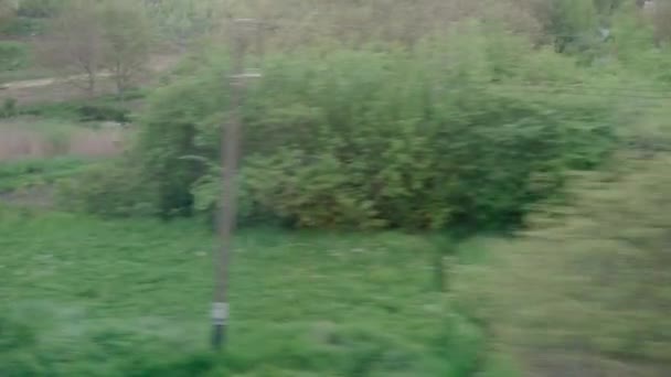 Vista da janela do trem de alta velocidade na paisagem de casas de aldeia de campo de natureza bonitas e floresta no pôr do sol de céu crepúsculo da tarde no contexto de verão. Transporte, viagens, ferrovia, conceito de comunicação — Vídeo de Stock