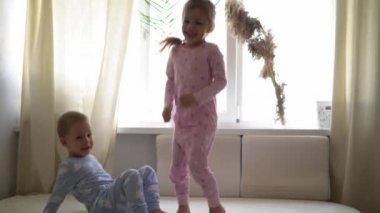 İki gülümseyen preshool, yeni yürümeye başlayan çocuk beyaz yatakta pijamalarıyla uzanan kız ve erkek çocuk. Kardeş ikizler evde karantinada eğleniyor, mutlu çocuklar. Arkadaşlık, aile, eğitim kavramı