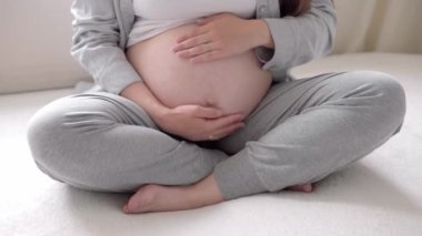 Evde karnına dokunan mutlu hamile bir kadın var. Şefkatli anne, güneşli bir yaz gününde çıplak, koca göbeğini, ışık odasındaki elleriyle okşar. gebelik, annelik, insanlar, beklenti