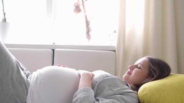 임신, 모성, 사람들, 기대 - 행복 한 피로에 지친 임산부가 배의 휴식 시간을 만지는 모습 - 집에서 보살펴 주는 어머니는 화창 한 날밝은 방에서 쉬는 자세로 침대에 누워 있다 — 비디오
