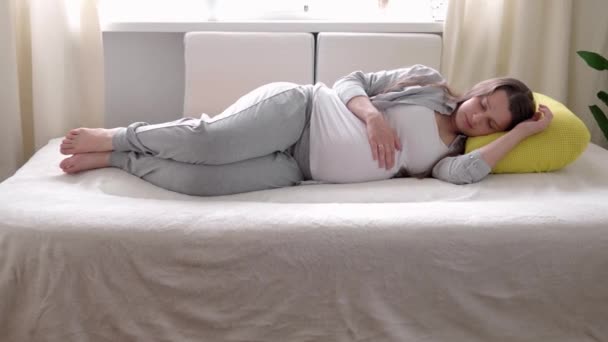 Terhesség, anyaság, emberek, elvárás koncepció - boldog fáradt álmos terhes nő megérinti a pocakját alvás pihen az ágyban otthon gondoskodó anya pihenjen stroke hason fény szoba napsütéses napon — Stock videók