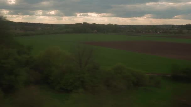Widok z okna pociągu dużych prędkości na krajobraz pięknej przyrody zielone pole i las na wieczór zachmurzone zmierzch niebo zachód słońca w tle lata. Transport, podróże, kolej, koncepcja komunikacji — Wideo stockowe