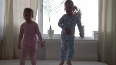 İki gülümseyen preshool, yeni yürümeye başlayan çocuk beyaz yatakta pijamalarıyla uzanan kız ve erkek çocuk. Kardeş ikizler evde karantinada eğleniyor, mutlu çocuklar. Arkadaşlık, aile, eğitim kavramı