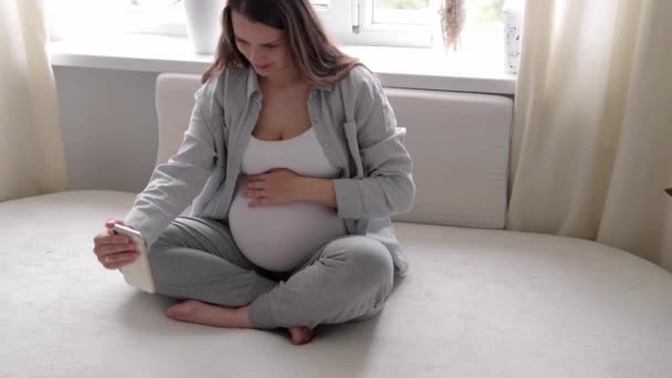 Glad gravid kvinde med tablet har videoopkald ved hjælp af smartphone kommunikerer med mand via chat online konsultation med læge tale med venner på mobiltelefon. graviditet, teknologi, medicin – Stock-video