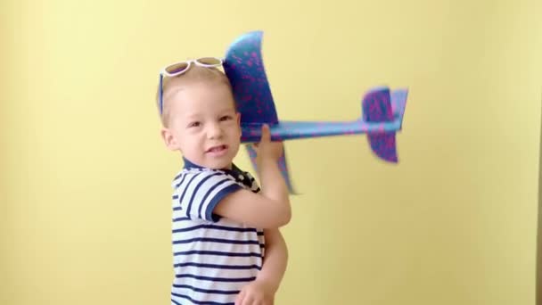 Kleine Vorschulkinder in blauem T-Shirt spielen mit Plastikschaumflugzeug auf gelbem Hintergrund. Kinder imitieren fliegende Flugzeugattrappen. Urlaub, Sommerberuf, Kindheitsreise — Stockvideo