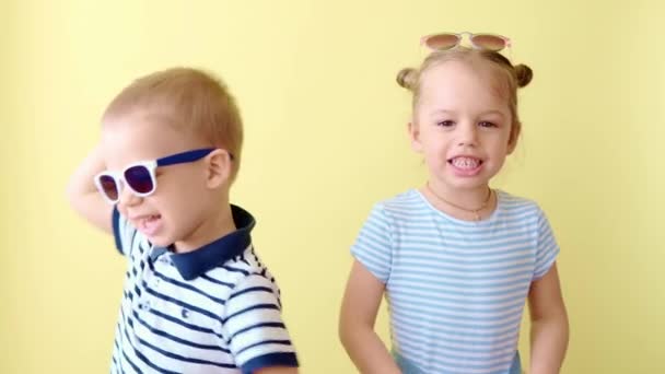 Familie, vriendschap, kindertijd, zomer. Twee blije Indrukwekkende glimlachende peuter kinderen broer of zus dans vieren spelen veel plezier lachen. Grappige kinderen in bril broer zus op geel kopiëren ruimte achtergrond — Stockvideo