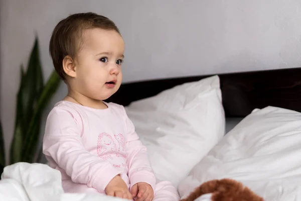 Auténtico retrato lindo bebé caucásico regordete niña o niño en rosa somnoliento al despertar mirando a la cámara en la cama blanca. Cuidado de niños, Infancia, paternidad, concepto de estilo de vida — Foto de Stock