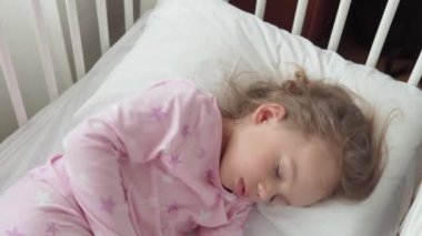 Otantik, beyaz, küçük, beyaz, beyaz bir beşikte küçük, beyaz bir anaokulu kızı öğle yemeği vaktinde yatak odasında tatlı tatlı uyur. Çocuk dinleniyor. Pencerenin yanındaki yatakta uzanıyor. Çocukluk, tıp, sağlık konsepti