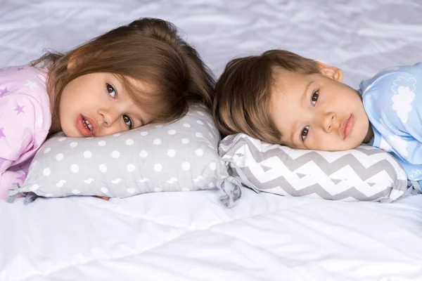Hem, komfort, barndom, sömnlöshet, sömnlöshet, söt dröm - två ledsna trött småbarn syskon barn tvillingar i pyjamas ligga vila kan inte sova på sängen kuddar titta på kameran mjuk mysig sömnig stämning — Stockfoto