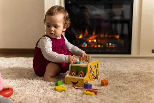 어린이, 발달, 기술, 무기력 한 놀이 - 거의 진짜 아기가 걸음마를 하는 여자 아이는 아늑 한 집 거실에 있는 매트 카펫 바닥에 앉아 나무로 만든 장난감 차우더를 연주하는 색깔의 인형 모양을 만들어 낸다 — 스톡 사진