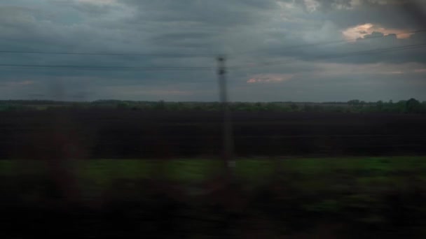 Vista da janela do trem de alta velocidade na paisagem de belo campo selvagem de natureza e floresta em pôr do sol de céu de crepúsculo nublado da tarde em fundo de verão. Transporte, viagens, ferrovia, conceito de comunicação — Vídeo de Stock