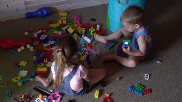 Μικρά παιδιά προσχολικής ηλικίας που κάθονται στο πάτωμα με παιχνίδια σε παιδικό δωμάτιο. Τα παιδιά παίζουν με τον κατασκευαστή στο playroom. Τα παιδιά έχουν περάσει καλά στο σπίτι. Παιδική ηλικία, φιλία, έννοια της ανάπτυξης — Αρχείο Βίντεο