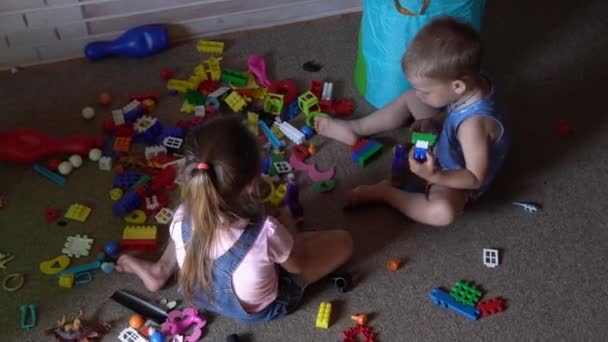 Pequeños hermanos preescolares niños sentados en el suelo con juguetes en la habitación de los niños. chicos están jugando con constructor en la sala de juegos. los niños han pasado un rato divertido en casa. Infancia, amistad, concepto de desarrollo — Vídeo de stock