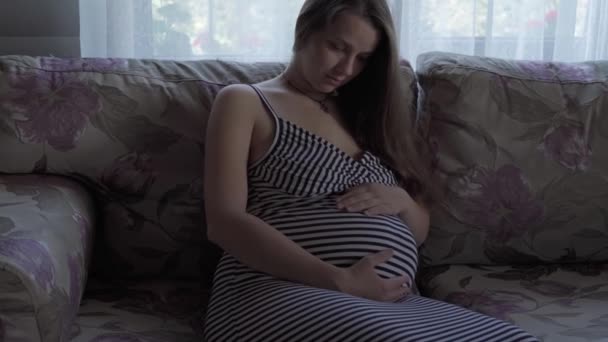 Cute happy tired pregnant woman touching her tummy resting sitting in bed at home. caring mother take rest stroke belly on light provence style room. pregnancy, motherhood, people, expectation concept — Stock Video