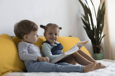 İki küçük çocuk sarı yatakta büyük, ilginç peri masalları kitabı okuyor. Kardeş ikizler evde karantinada eğleniyor, mutlu çocuk. Arkadaşlık, aile, eğitim kavramı