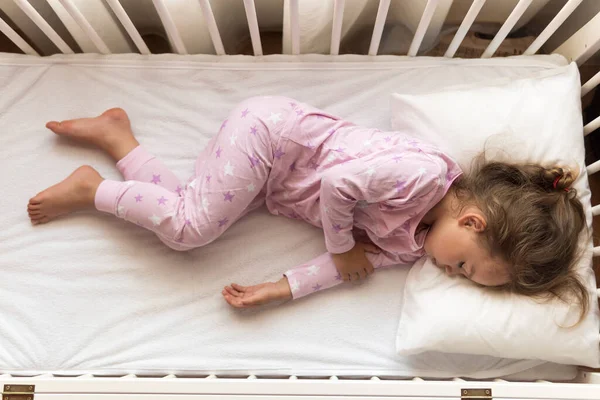 Вид сверху Милый маленький 3-4 лет дошкольного ребенка девочка спит сладко в белой кроватке во время обеденного отдыха в розовой пижаме с подушкой дома. Детство, отдых, комфорт, медицина, концепция здоровья — стоковое фото