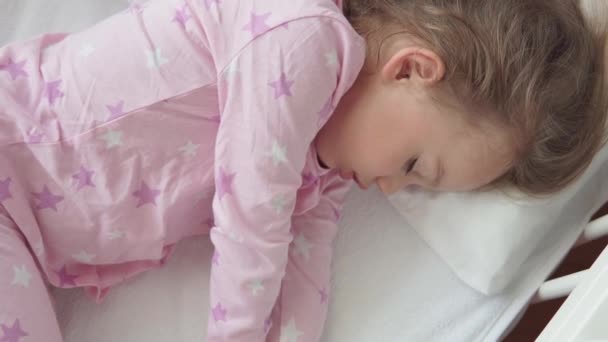 Nahaufnahme authentische niedliche kaukasische kleine Vorschulkind Mädchen schlafen süß in weißen Krippe auf Pyjama im Schlafzimmer während der Mittagszeit. Kind liegt im Bett neben Fenster. Kindheit, Medizin, Gesundheitskonzept — Stockvideo