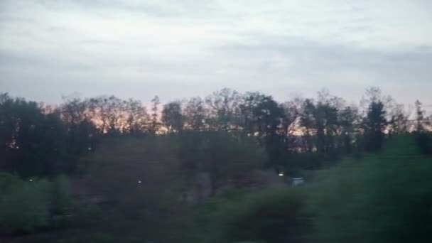 View from window of high-speed train on landscape of beautiful nature field village houses and forest on evening dusk sky sunset in summer background. Transport, travel, railway, communication concept — Stock Video