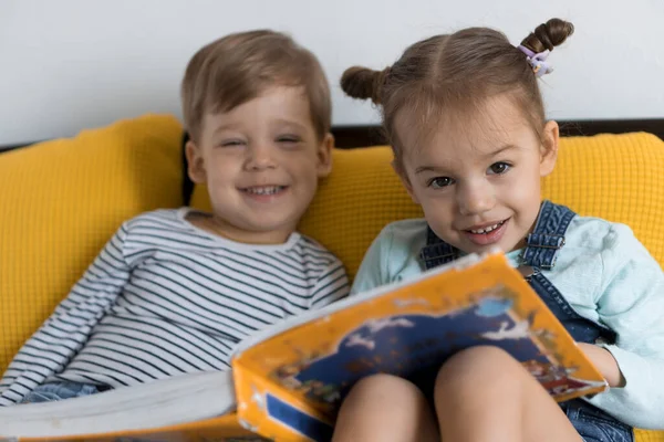 Deux enfants d'âge préscolaire, tout-petits lire grand livre intéressant de contes de fées sur lit jaune. Frères et soeurs les petits jumeaux lecteur ont plaisir, enfant heureux en quarantaine à la maison. Amitié, famille, concept d'éducation — Photo