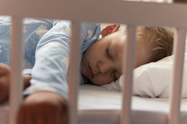 2-3 yaş arası sevimli, kreş çocuğu öğle yemeği arasında evinde yastıklı mavi pijamayla beyaz karyolada tatlı tatlı uyuyor. Çocukluk, rahatlık, rahatlık, ilaç, sağlık konsepti