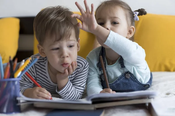 Intelligent souriant préscolaire tout-petit enfants garçon et fille dessiner avec des crayons couchés sur le ventre au lit jaune. petit lecteur mignon amusez-vous, enfant heureux en quarantaine à la maison. Amitié, famille, éducation — Photo