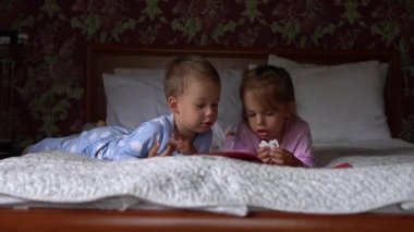 İki sevimli, gülümseyen preshool, pijamalı çocuk yatakta masal kitabı okuyor. Kardeş küçük ikiz okuyucular eğleniyor. Mutlu çocuklar evde karantinada. Arkadaşlık, aile, eğitim kavramı