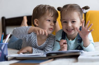 Zeki, gülümseyen, küçük bir çocuk çocuk ve kız sarı yatakta göbeklerinde kalemlerle resim yapıyorlar. Küçük sevimli okuyucu evde karantinada eğleniyor, mutlu çocuk. Arkadaşlık, aile, eğitim.